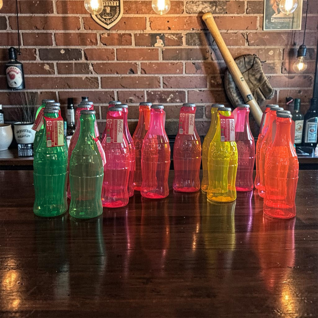 Southern Charm Collectibles neon-colored translucent plastic Coca-Cola decorative bottles on a wooden bar top